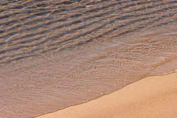 The receding gentle waves of Lake Michigan off the berach within Kohler-Andrae State Park, Sheboygan, Wisconsin, the clear water displaying the shallow ripples beneath the surface.