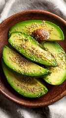 Top down view of neatly sliced avocado arranged on a bamboo plate, garnished with seeds, set against a neutral linen backdrop.