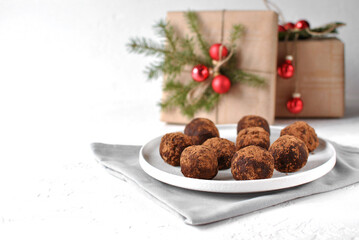 Chocolate truffles dusted with cocoa sit on a white plate beside wrapped gifts and evergreen sprigs for a cozy holiday scene.