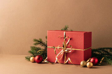 Christmas red gift, fluffy fir branches, golden sparkling streamers and Christmas tree decorations, beige minimalist background