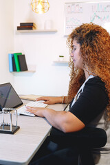 Vertical photo of awoman with curly red hair working on a tablet with wireless keyboard in modern office