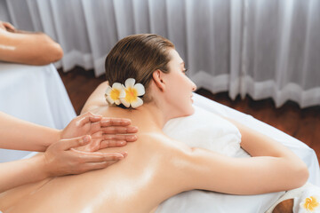 Caucasian couple customer enjoying relaxing anti-stress spa massage and pampering with beauty skin recreation leisure in day light ambient salon spa at luxury resort or hotel. Quiescent