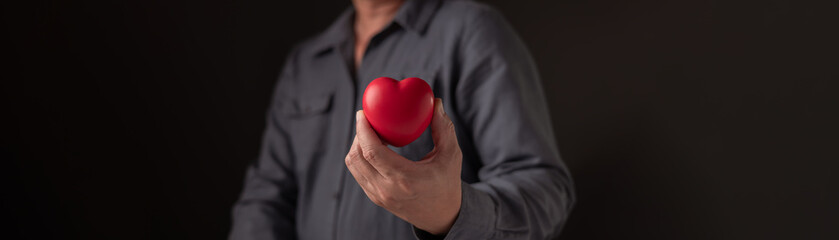 Man hand holding red heart shape on dark background. Concept of love, healthcare, medical insurance...