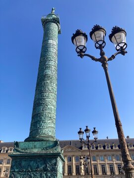 Vend&ocirc;me-S&auml;ule in Paris mit verzierten Laternen vor strahlend blauem Himmel am Place Vend&ocirc;me
