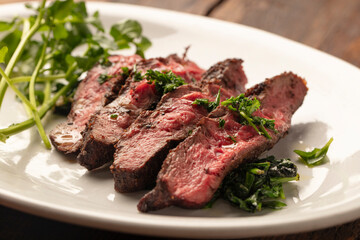 Medium-rare sliced steak on a white plate with microgreens—a rustic wood table surface. 