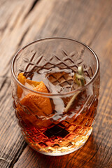Close-up shot of an old-fashioned whiskey cocktail in a short glass with an orange peel on a rustic wood table. 