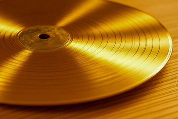 A brightly lit close-up of a shiny gold vinyl record lying on a warm wooden tabletop.
