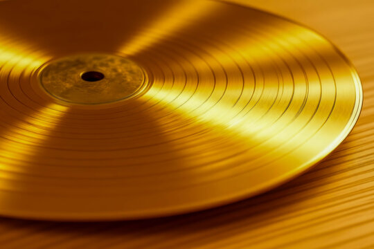 A brightly lit close-up of a shiny gold vinyl record lying on a warm wooden tabletop.