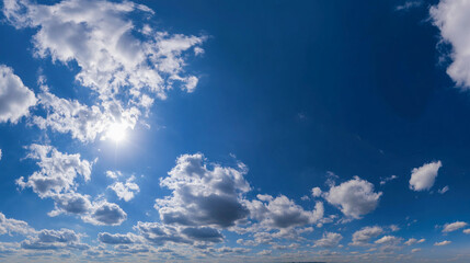 Sun shining brightly through the fluffy white clouds in a vibrant blue sky on a beautiful summer day