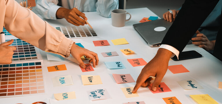 A vibrant workspace showcasing a team engaged in a brainstorming session. Colorful sticky notes and swatches reflect creative planning and collaboration efforts. SACTR