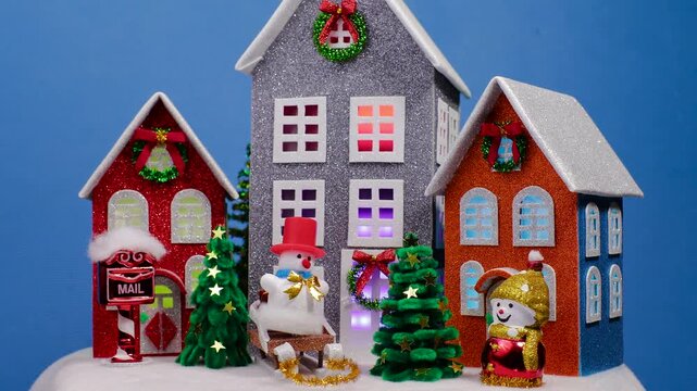 A Christmas house with large houses surrounded by small Christmas trees and snowmen on sleds and without them rotating on a blue background
