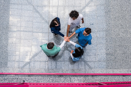 Diverse Medical Team Stacking Hands in Hospital Top View of Doctors and Nurses in Scrubs Showing Teamwork and Unity. - Powered by Adobe