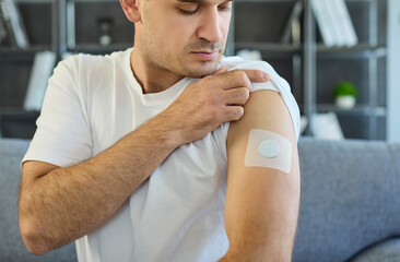 Man shows arm patch for diabetes sensor. The glucose monitor is a wearable medical device for...