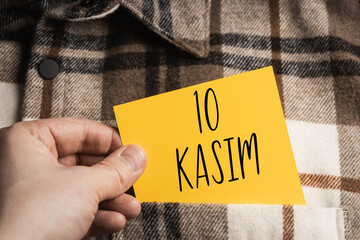 Turkish Remembrance Day November 10 (10 Kasim) - a yellow note held in the hand against the background of a brown and beige plaid shirt, symbolizing respect and a historical event