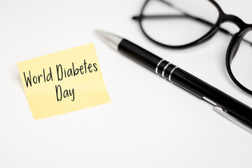 World Diabetes Day Concept with a yellow sticky note, glasses and a pen on a white background, a reminder of global health awareness.