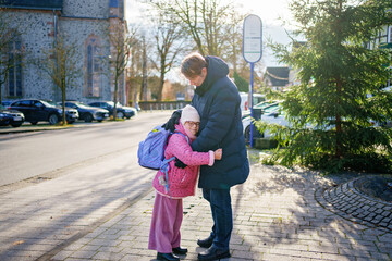 Little girl walking home from school with big bag. Her father meet her on the way. Walking together.