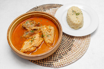 Kedjenou de poulet servi dans des récipients en terre cuite sur set tissé africain. Spécialité ivoirienne. Ragout de viande. Cuisine africaine traditionnelle. Traiteur africain.
