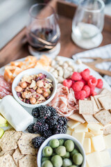 Charcuterie board with wine, fresh berries, cheese, crackers, and nuts on a wooden tray