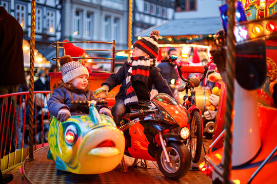 Adorable little boy and girl, siblings on a carousel at Christmas funfair or market, outdoors. Happy children, friends having fun. Selective focus on one child. Holiday, children, lifestyle concept.