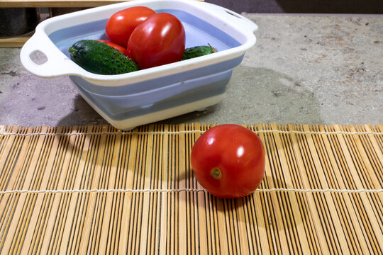 Ripe red tomato on bamboo mat. Red tomatoes and green cucumbers lie in plastic colander on the kitchen table. Real photo - Powered by Adobe