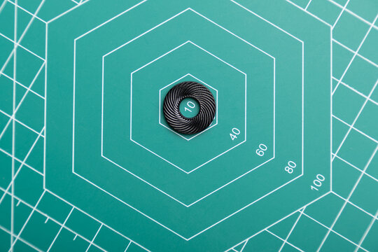 A black serrated lock washer is centered on a green hexagonal cutting mat with white guide lines. The concentric patterns highlight precision engineering, measurement, and crucial fastening components