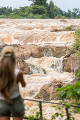 Woman traveling watching powerful waterfall and muddy river