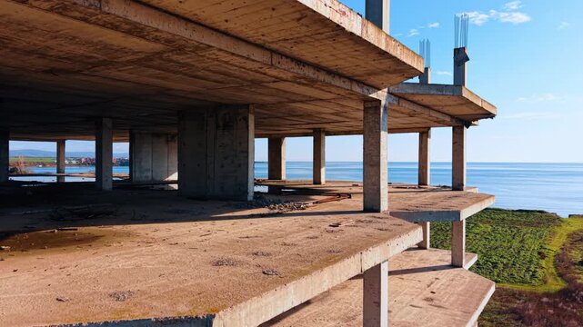 Flight through the structure of the abandoned unfinished multi-storied building. Amazing scenery of the seascape at backdrop.