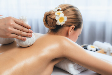 Naklejka premium Hot herbal ball spa massage body treatment, masseur gently compresses herb bag on woman body. Tranquil and serenity of aromatherapy recreation in day lighting ambient at spa salon. Quiescent