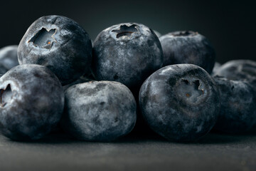 Macro close-up of ripe blueberries with a natural waxy bloom. Dark, moody food background with shallow depth of field.