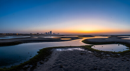 Fototapeta premium Serene Coastal Landscape at Sunrise with City Skyline Silhouette and Calm Waters
