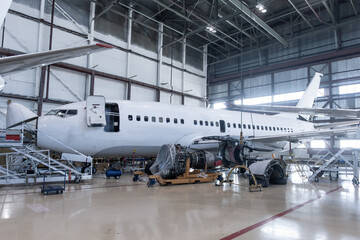 White passenger airplane under maintenance has opened weather radar and engine removed located nearby in the aircraft hangar