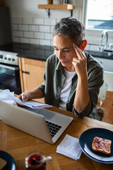 Mature woman stressed paying bills at home kitchen