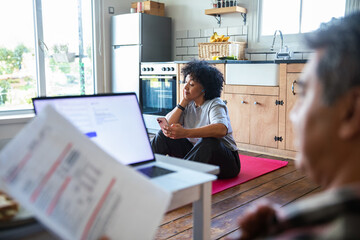 Adult woman stressed with smartphone and bills in home kitchen