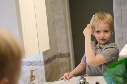 Young boy combing blonde hair in bathroom mirror