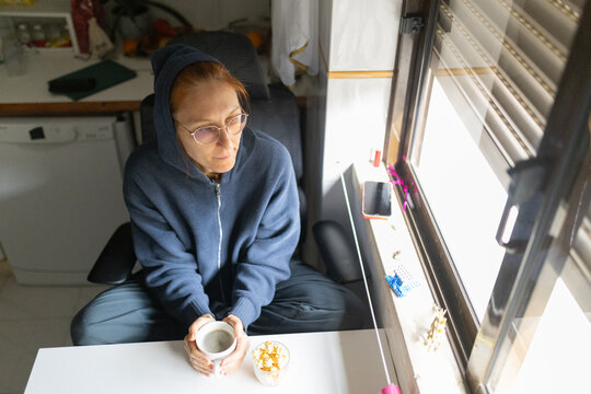 Woman wearing hoodie relaxing with coffee looking out window