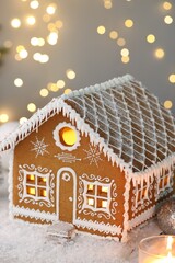 Beautiful gingerbread house and Christmas decor on table against blurred lights, closeup. Bokeh effect