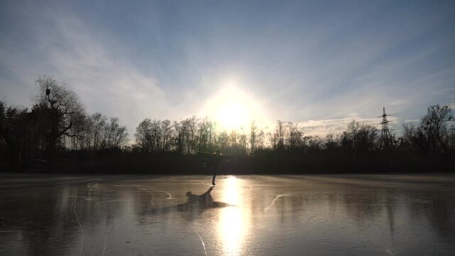 Young female figure skater training choreography on ice. Female sportsman enjoying sport in cold weather with sunlight reflected in beautiful icy surface of frozen lake. Girl training alone outdoor