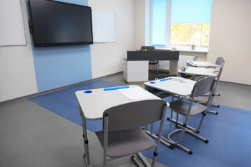 Stylish classroom with desks, chairs and tv at school
