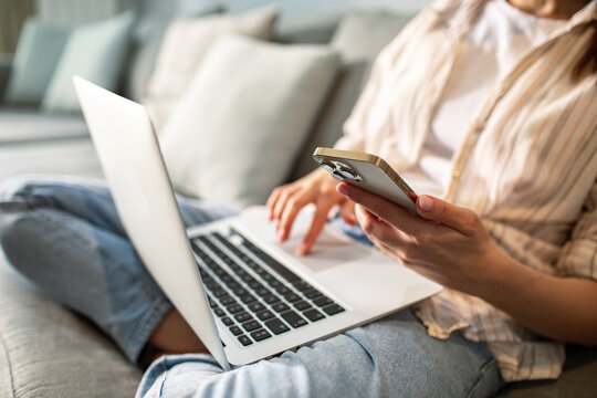 Young adult woman focused multitasking with smartphone and laptop at home