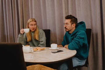 A young man and his female friend chat over tea in a cozy kitchen. Authentic moment of casual conversation and friendly connection in everyday setting