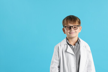 Cute little boy in laboratory coat and glasses on light blue background, space for text. Child and...