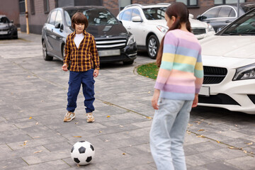 Little girl and boy playing with ball on parking outdoors. Children in danger