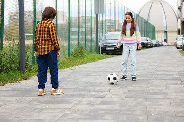 Little girl and boy playing with ball on pavement outdoors. Children in danger