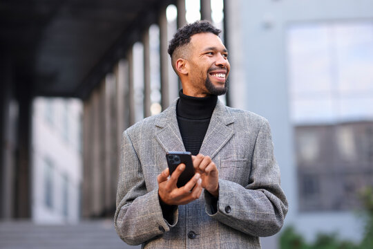 Smiling man in suit with smartphone on city street