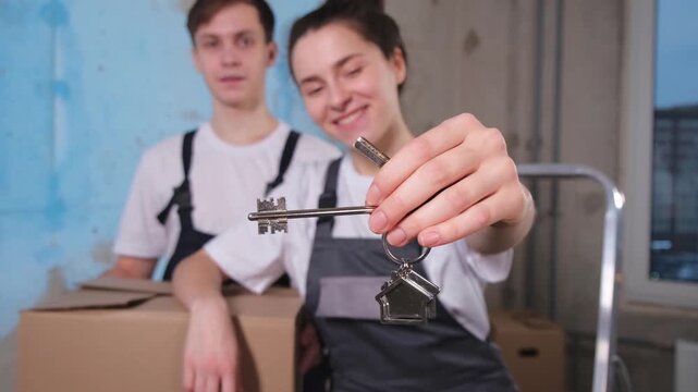 Own home. Mortgage relocation concept. Happy couple holding key from new first house. Family celebrating moving day. Husband wife customers buyers purchase real estate hold moving box showing keys