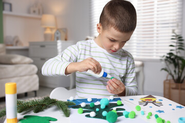 Little boy making Christmas postcard at table indoors. Child handmade craft
