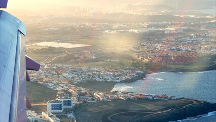 Obraz premium Airplane wing capturing an aerial view of the coastal town and residential areas of Gran Canaria, Canary Islands, during a warm sunset, symbolizing travel and holiday destinations