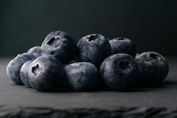 Still life of fresh blueberries on a dark surface with soft natural light and shallow depth of field. Healthy food concept with copy space.