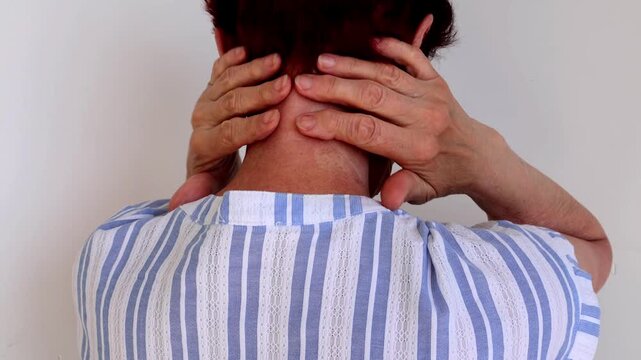A senior woman rubs her collar and neck area, relieving arthritis tension with slow, mindful self-massage.