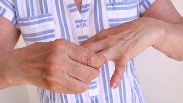 Older woman massages fingers and palms to manage arthritis pain and maintain mobility in aging hands.
